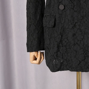 Close-up of black floral lace texture on a tailored suit jacket with button and pocket