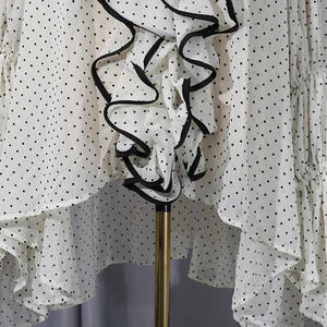 Close-up of white chiffon blouse featuring black polka dots and tiered ruffle details