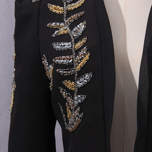 Macro detail of elaborate gold and silver bead embroidery on black suit jacket fabric