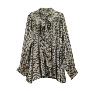 Close-up of geometric labyrinth pattern on gold chiffon shirt with luxury tie-neck detail