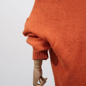 Detail of bright orange chunky knit oversized sleeves with ribbed cuffs and soft texture