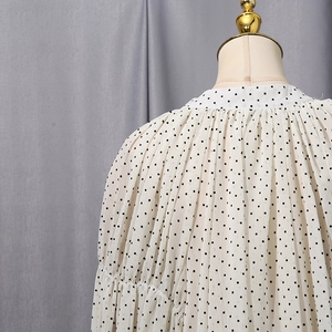Detail view of the elegant ruffled high neck and pleated shoulders on a polka dot blouse