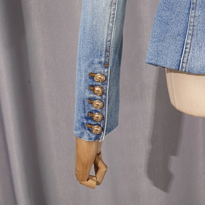 Close-up of light blue denim sleeve featuring five decorative golden lion embossed buttons