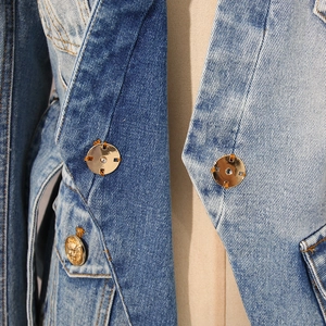 Detailed macro shot of vintage lion head embossed gold button on patchwork denim jacket