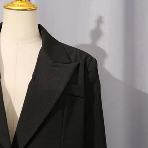 Close-up of peaked lapel and flap pocket on a fitted black blazer with refined texture