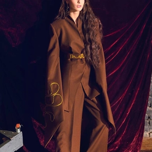 Detailed embroidery with gold linear patterns on dark brown suit sleeves and waist belt