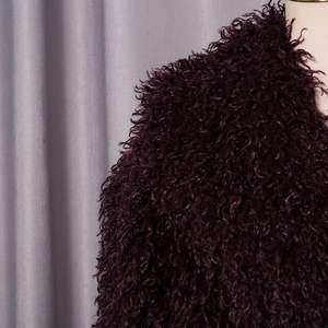 Macro shot showing texture of dark purple faux fur coat with thick curly wool fibers