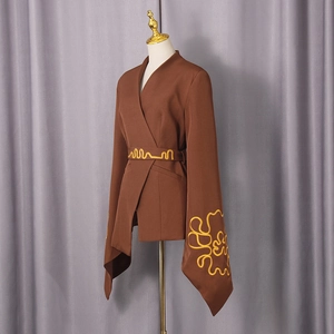 Detail of dark brown blazer featuring wide sleeves and bright yellow curved embroidery