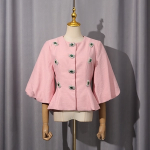 Dettaglio della giacca peplum rosa con bottoni in strass smeraldo e tessuto strutturato