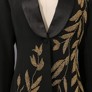 Détail de la broderie de blé dorée et du revers en satin sur un blazer noir chic