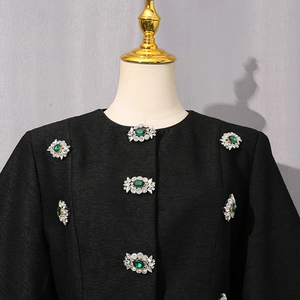 Dettaglio dell'elegante camicetta nera con bottoni gioiello verde smeraldo e tessuto