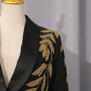 Détail de broderie de perles dorées sur le revers en satin noir d'une veste de blazer