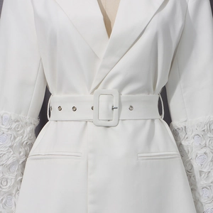 Détail d'un manteau blanc avec des fleurs 3D sur les manches et une ceinture à boucle chic