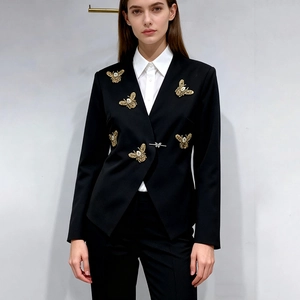 Détail d'un blazer noir cintré avec broderie d'abeille dorée et fermoir papillon argenté