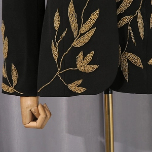 Détail de broderies dorées en forme de feuilles et perles sur veste de costume noire