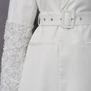 Détail d'une manche de manteau blanc avec pétales de rose 3D, paillettes et large ceinture