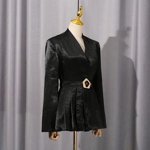 Détail d'un blazer en satin avec une boucle dorée en pentagone sur la ceinture assortie