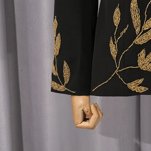 Détail de la broderie complexe de feuilles dorées sur le poignet d'un blazer noir