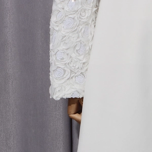 Détail d'appliqués de roses 3D et paillettes sur la manche d'un manteau blanc