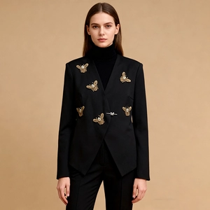 Détail du blazer noir sans col avec abeilles dorées et boucle papillon argentée