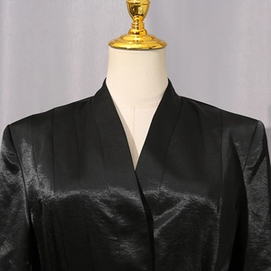 Détail d'un blazer en satin plissé noir avec col en V et texture de tissu satiné brillant