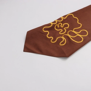 Detail of coffee-colored blazer cuff featuring gold abstract embroidery and textured fabric