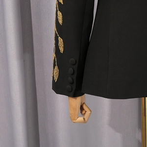 Détail de broderie de feuilles dorées et boutons assortis sur une manche de blazer noir