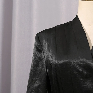 Détail du blazer en satin noir avec plis aux épaules et design chic à col en V