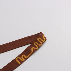 Close-up of brown woven fabric trim with yellow wavy embroidery and detailed stitch patterns