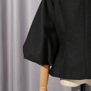 Dettaglio ravvicinato del tessuto nero strutturato e manica a sbuffo della camicia