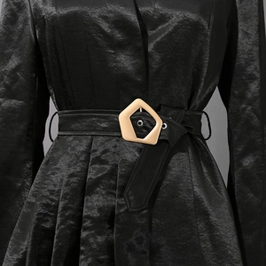 Détail d'un blazer noir en satin avec texture plissée et boucle de ceinture dorée