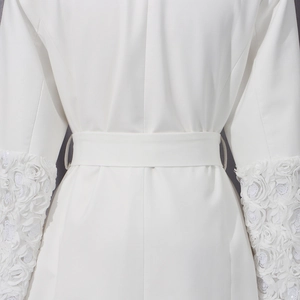 Détail d'un trench-coat blanc avec appliques florales 3D et paillettes sur la manche