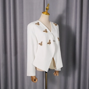 Détail d'abeilles en paillettes dorées cousues main sur un blazer blanc de luxe