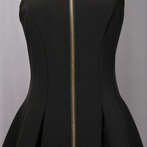 Detailed close-up of a black dress waist with a golden zipper and pleated fabric