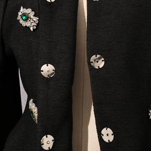 Dettaglio della trama in tweed nero con bottoni argentati e spille con smeraldo
