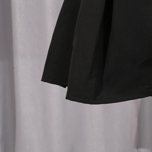 Detail view of the pleated black dress hem featuring precise stitching and woven fabric texture