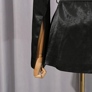 Détail des poignets fendus et texture du tissu brillant d'un blazer noir cintré