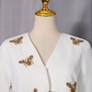 Détail d'un blazer blanc à col en V orné d'exquises appliques d'abeilles en strass dorés