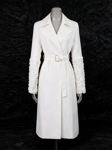 Trench-coat long blanc élégant avec fleurs 3D aux poignets et ceinture sur fond sombre