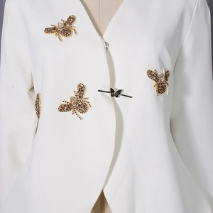 Détail d'un blazer blanc avec broderie abeille en perles et fermoir papillon unique