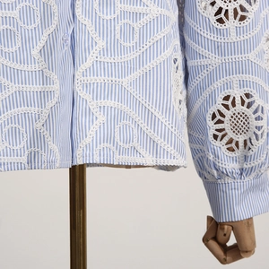Detail of blue striped shirt showing intricate white lace floral embroidery and fabric texture