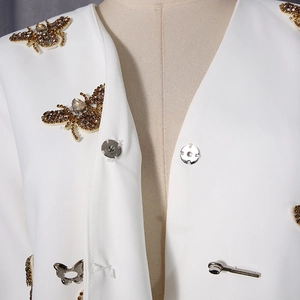 Détail d'un blazer blanc avec broderie d'abeille en paillettes et ornements en strass