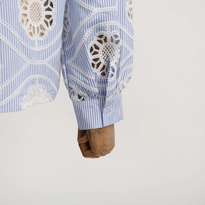 Detailed close-up of blue striped shirt sleeve with white lace cutout embroidery and button