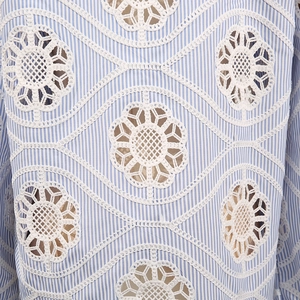Macro detail of striped blue fabric with elegant white floral embroidery and cutouts