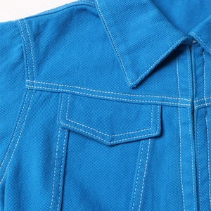 Dettaglio ravvicinato della giacca di jeans blu acceso con cuciture bianche e tasche a patta