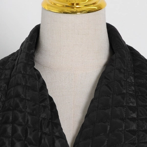 Detail view of black diamond quilted texture and glossy fabric on a women long jacket
