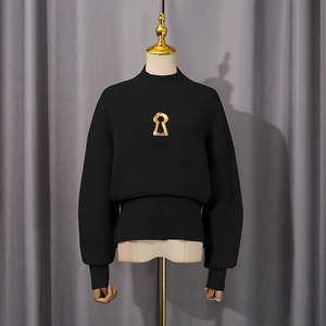 Detail of black turtleneck knit sweater with vertical ribbing and gold keyhole charm