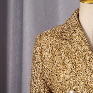 Detail of tweed blazer fabric with golden thread texture and white pearl button embellishment