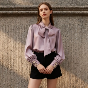 Détail d'un chemisier en satin lilas avec un grand nœud papillon et des boutons métalliques