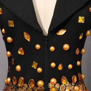 Detail eines schwarzen Kleides mit bernsteinfarbenen Steinen, Goldnieten und Pailletten